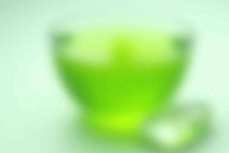 Élénkítő zöld tea egy elegáns japán teáscsészében, mellette egy ragyogóan áttetsző hegyikristály ásvány, világos, élénk környezetben.